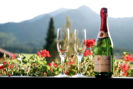 Sektflasche und zwei Sektgläser stehen auf dem Balkon vor Bergpanorama