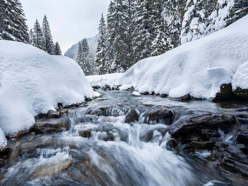 Fließender Bach in schneebedeckter Landschaft